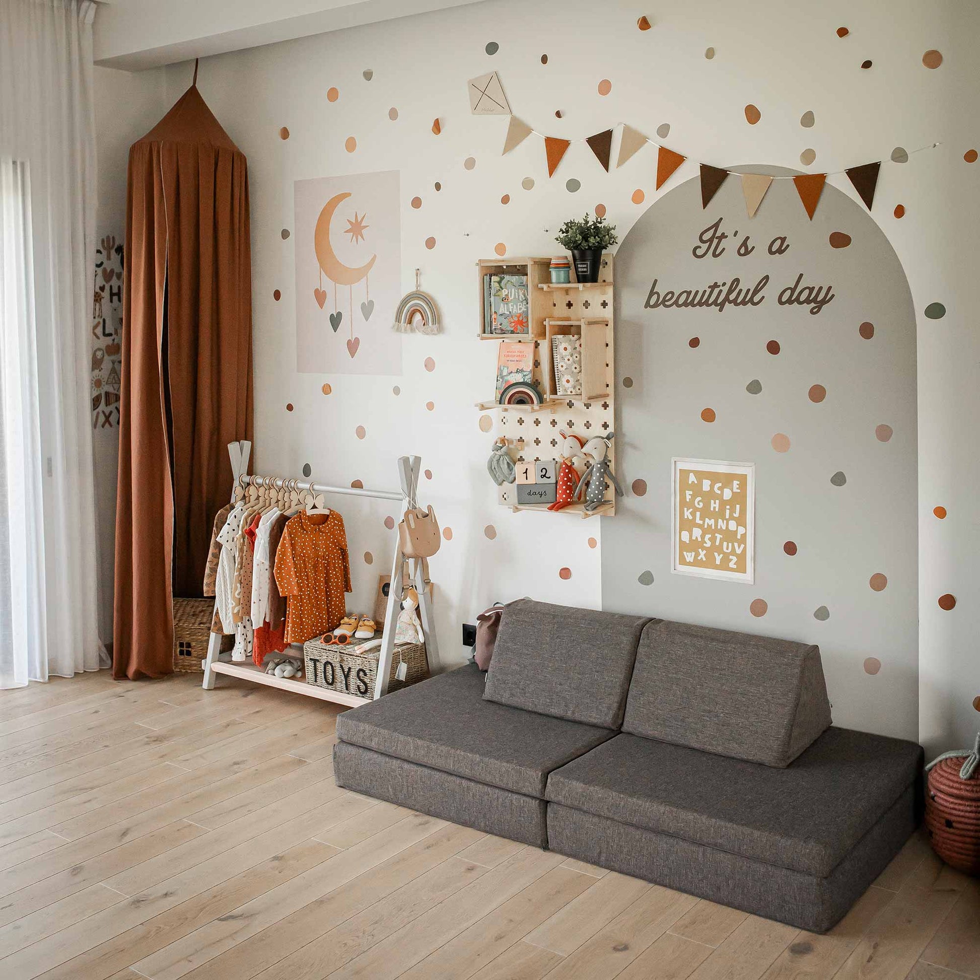A cozy children's room with a Monboxy Mattress set - Dark brown, a clothes rack, a wall decorated with polka dots, a canopy, shelves with toys for open-ended play, and various wall art, including a sign that reads “It’s a beautiful day.”