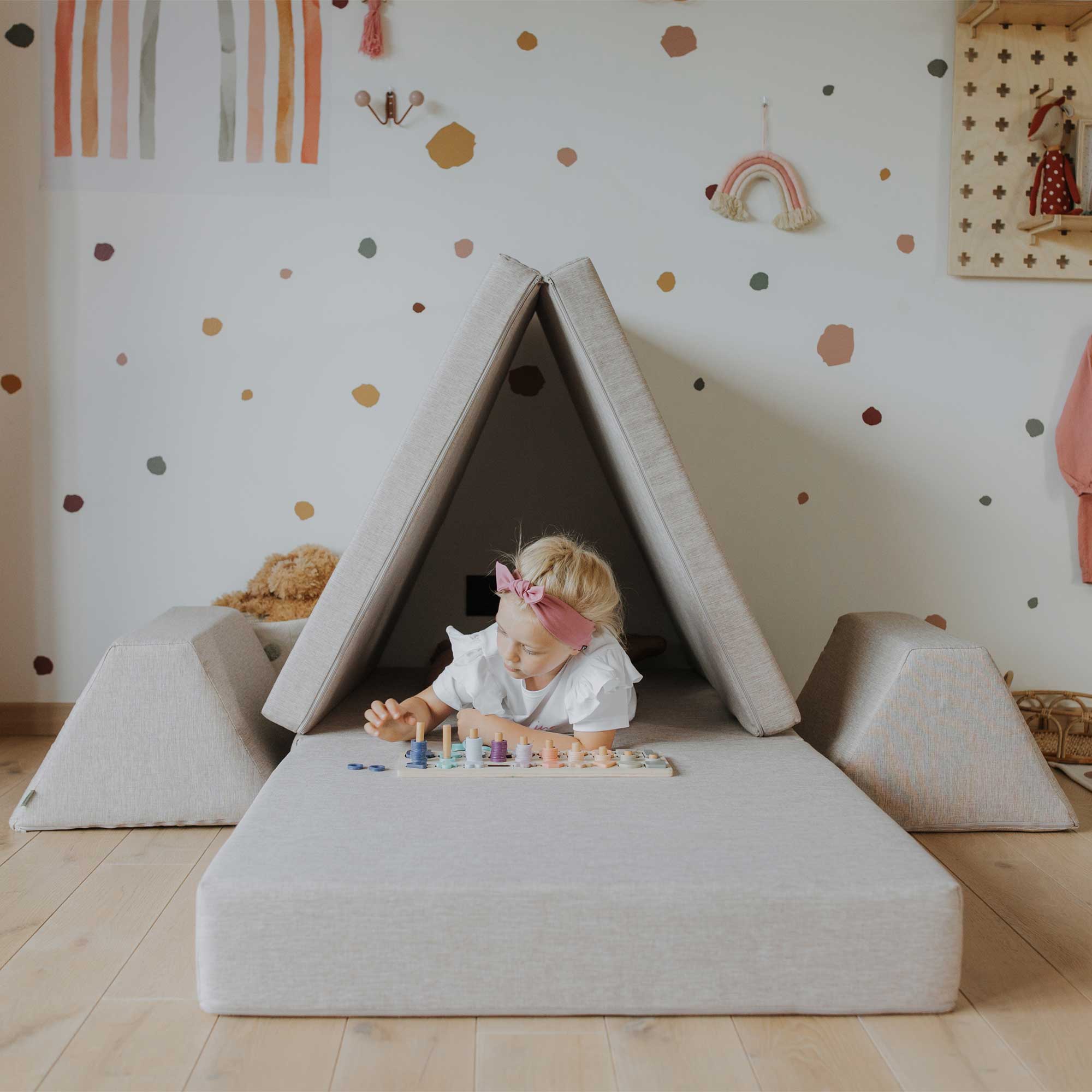 A girl playing with a wooden toy inside her beige Monboxy play couch for kid build as a wigwam