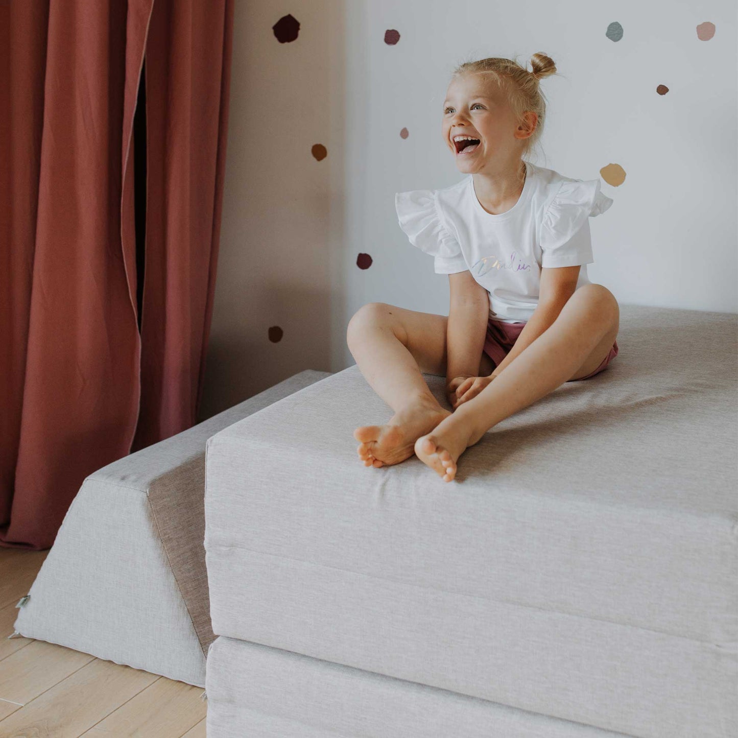 A girl laughing sitting on her beige Monboxy play mat or foam kid activity play set