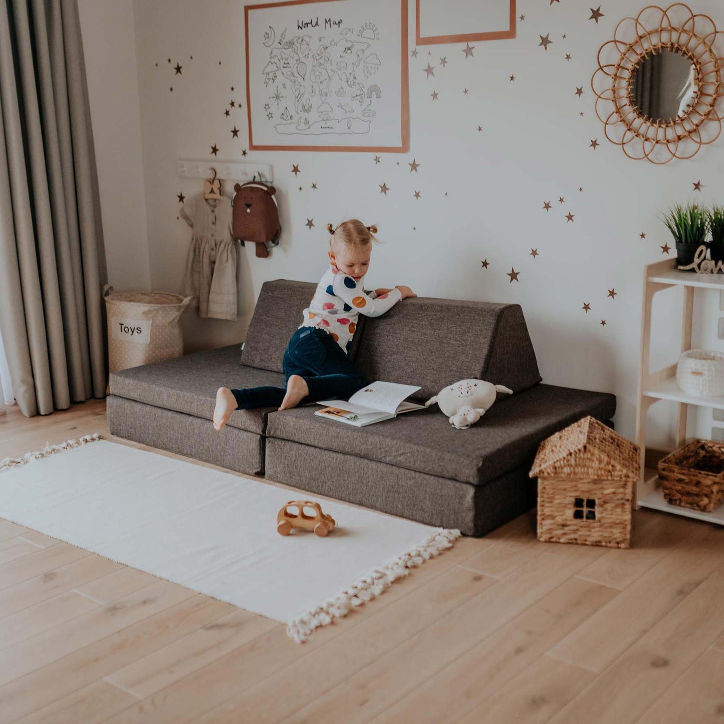 A young child reading a book on a Monboxy play couch in a neatly organized playroom with star decorations on the wall.