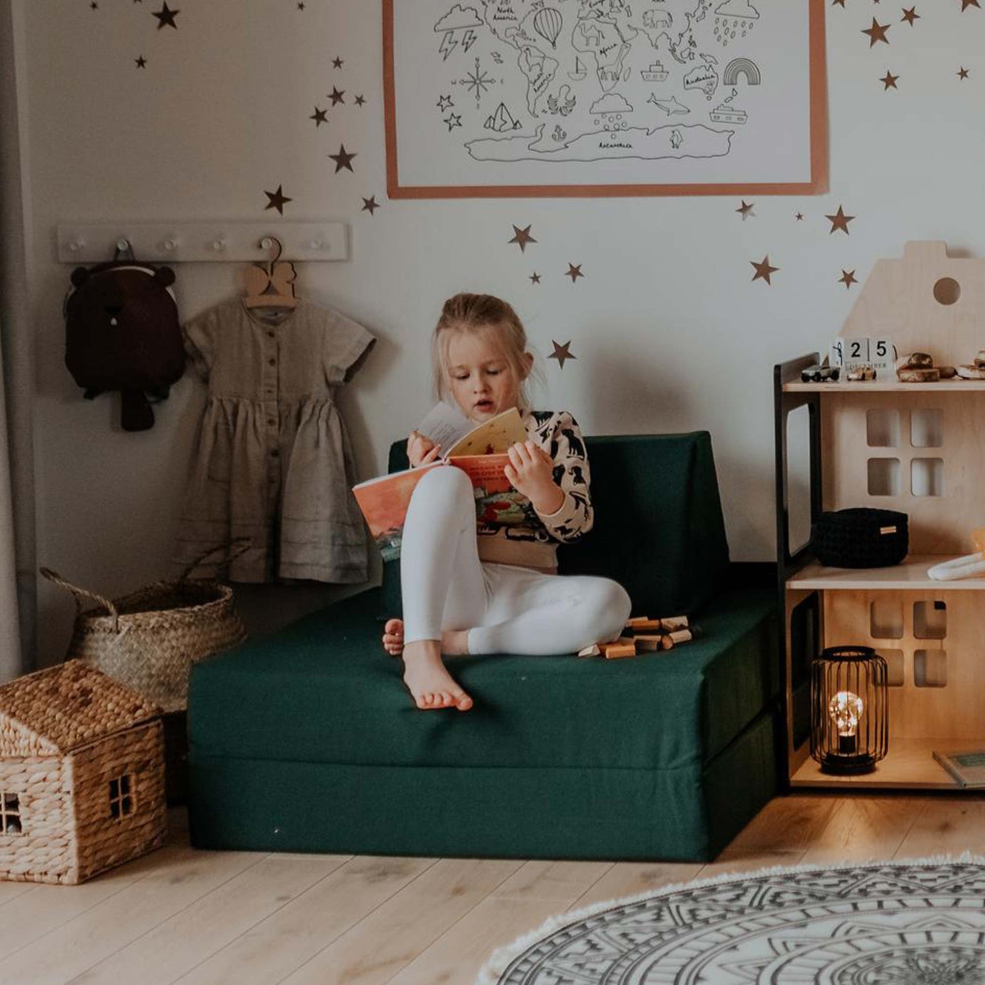A girl reading a book sitting on her deep green Monboxy sofa in her room
