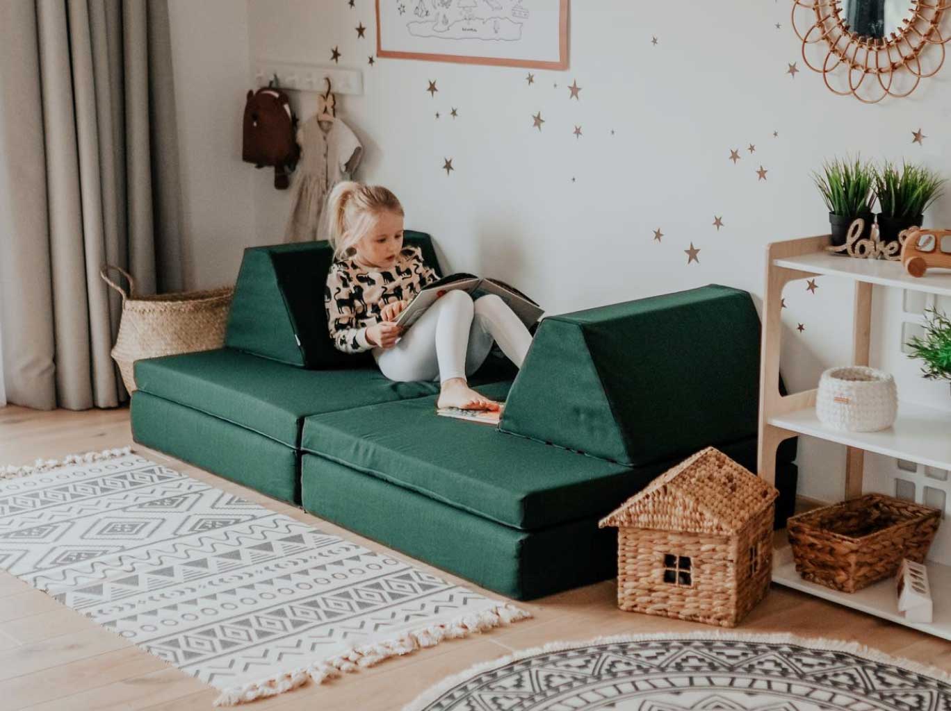 A toddler girl reading a book on her deep green Monboxy sofa set