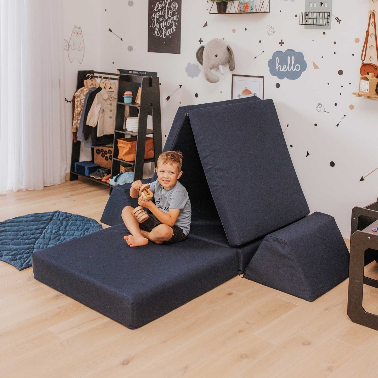 A boy playing with wooden toys inside a navy blue Monboxy foam activity mattress set