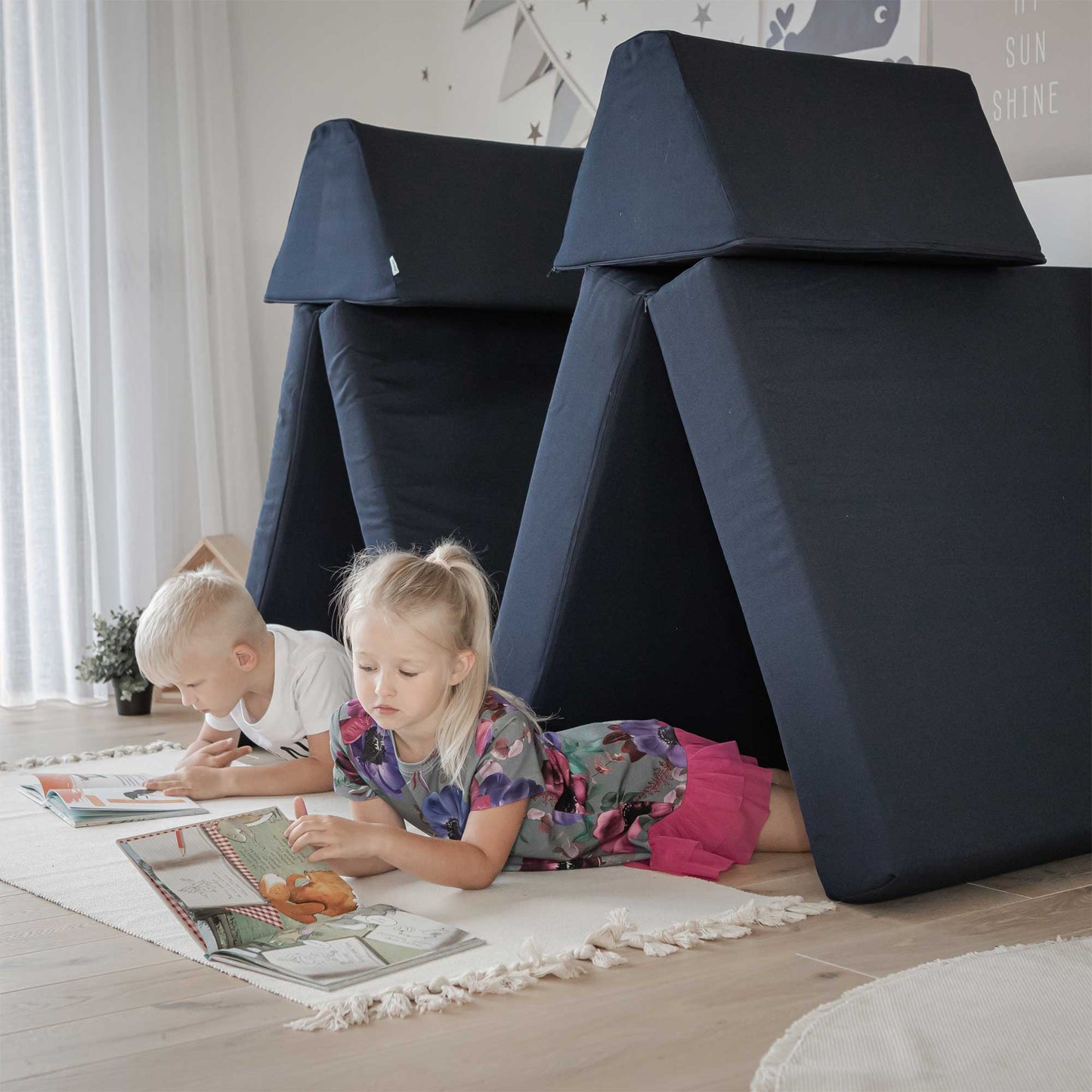 A girl and a boy laying on their tummies reading a book inside a navy blue soft foam wigwam