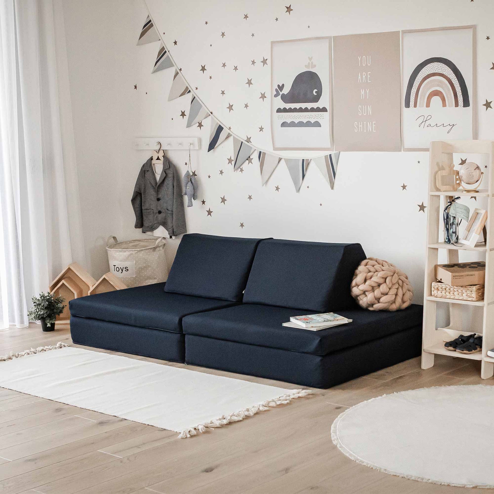 A neatly arranged children's playroom with a Montessori play couch, decorative wall hangings, and Monboxy soft blocks set in navy blue.
