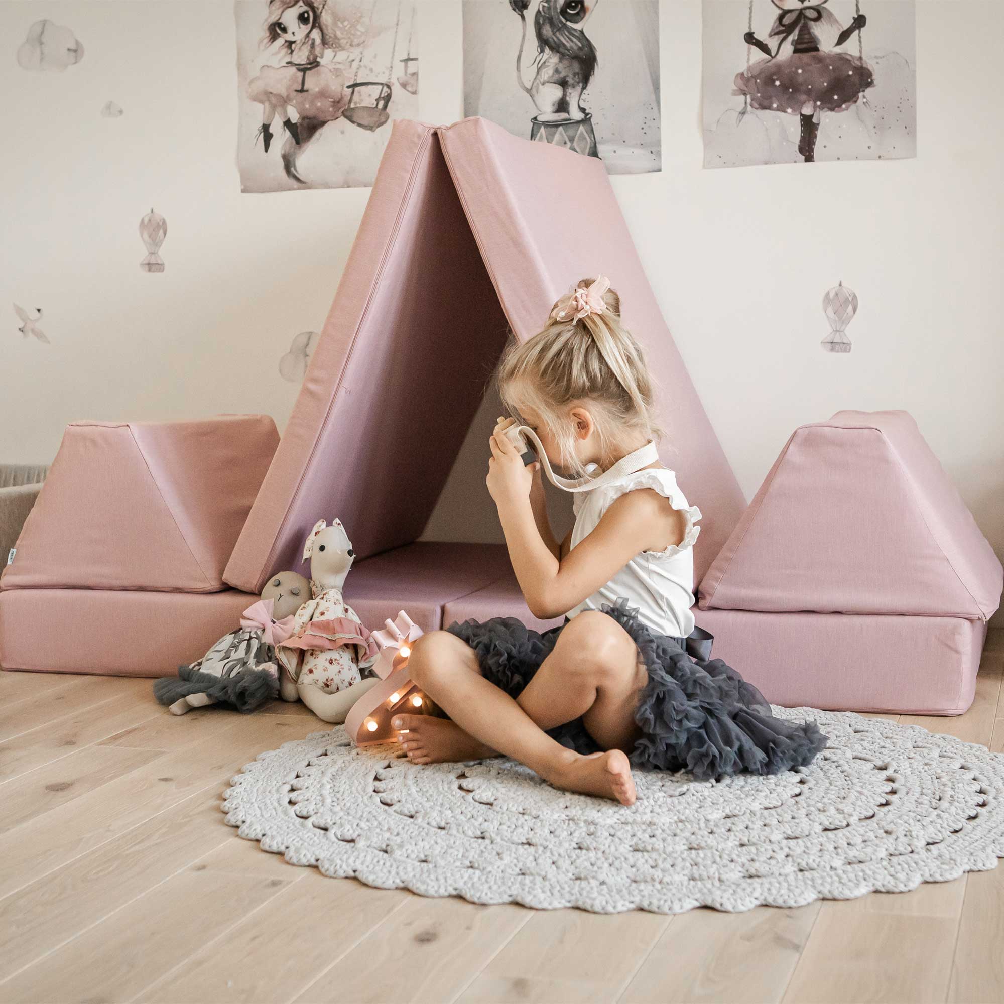 A girl playing with her toys next to a pink Monboxy play couch for kid put as a wigwam