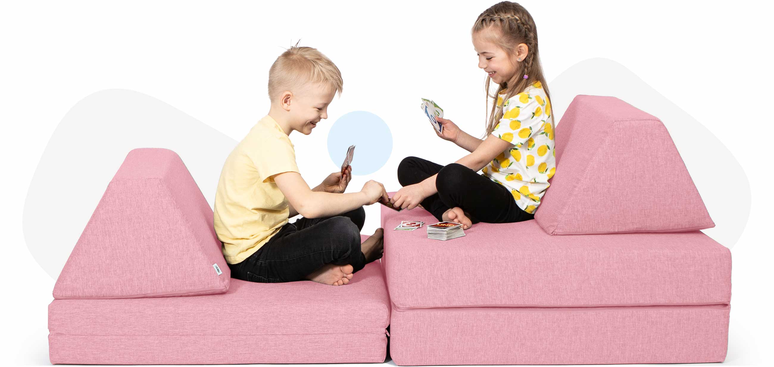 Kids sitting and playing cards on a pink Monboxy activity sofa