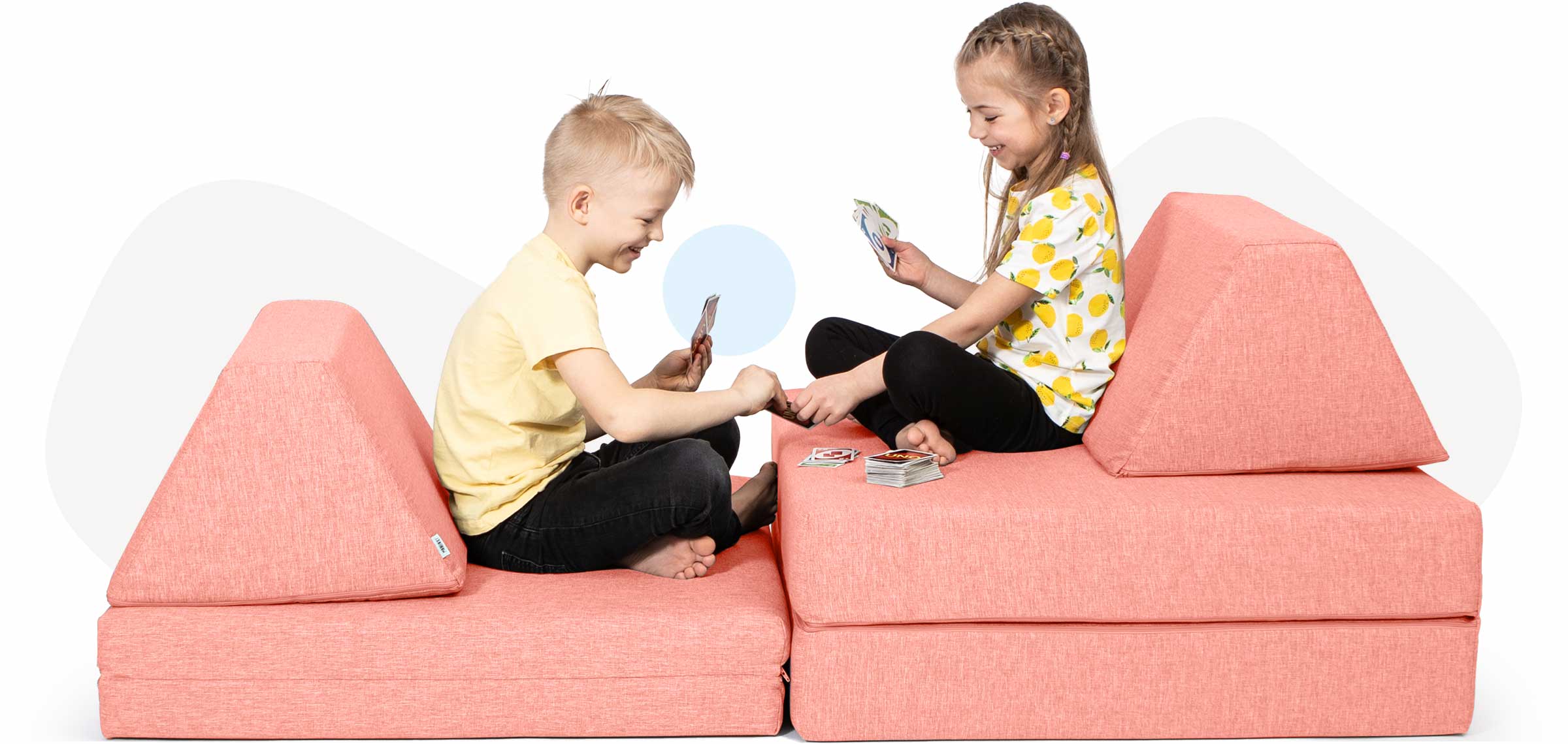 Two kids sitting on a salmon pink Monboxy spielsofa and playing cards