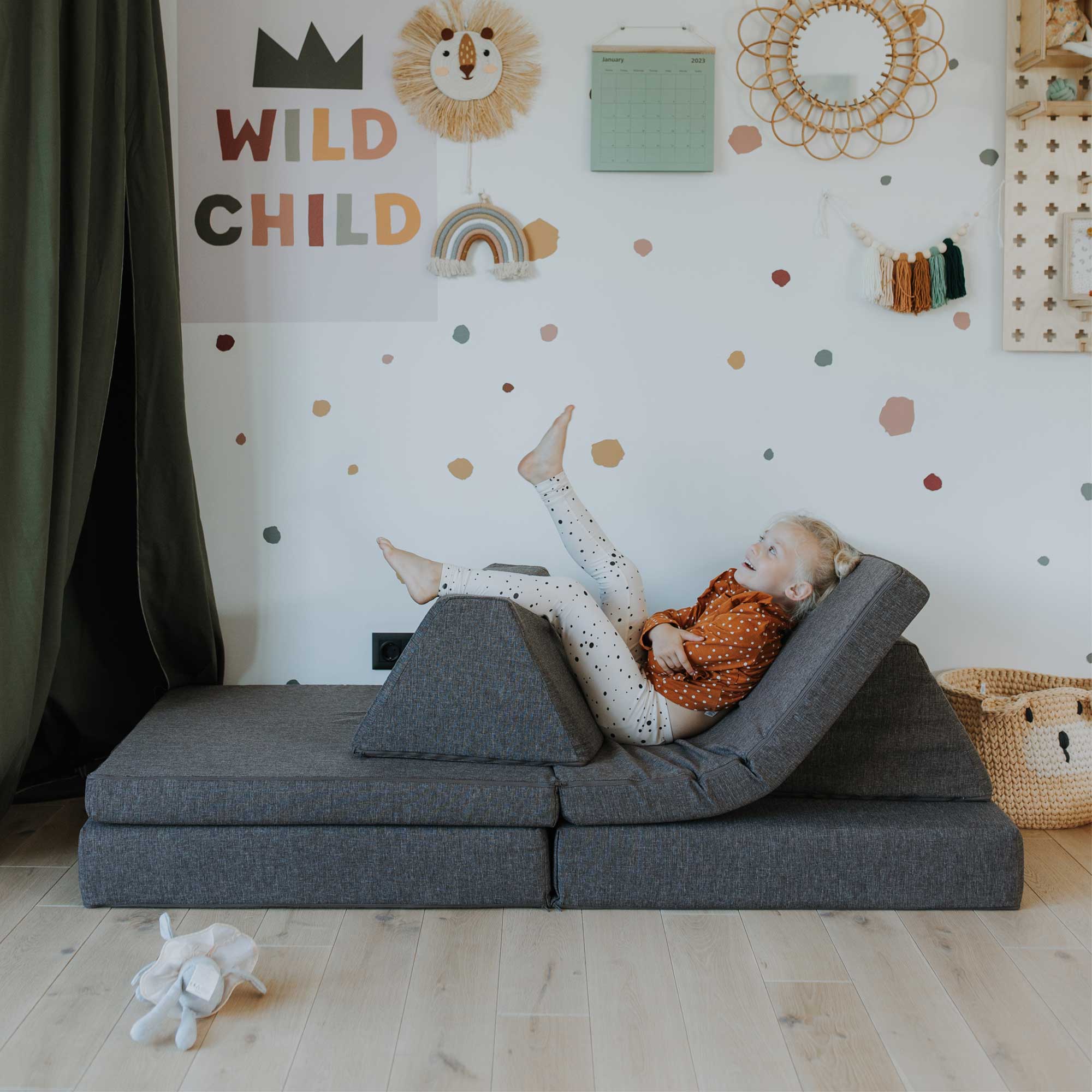 A little girl resting on a dark brown Monboxy play sofa set, arranged like a bed