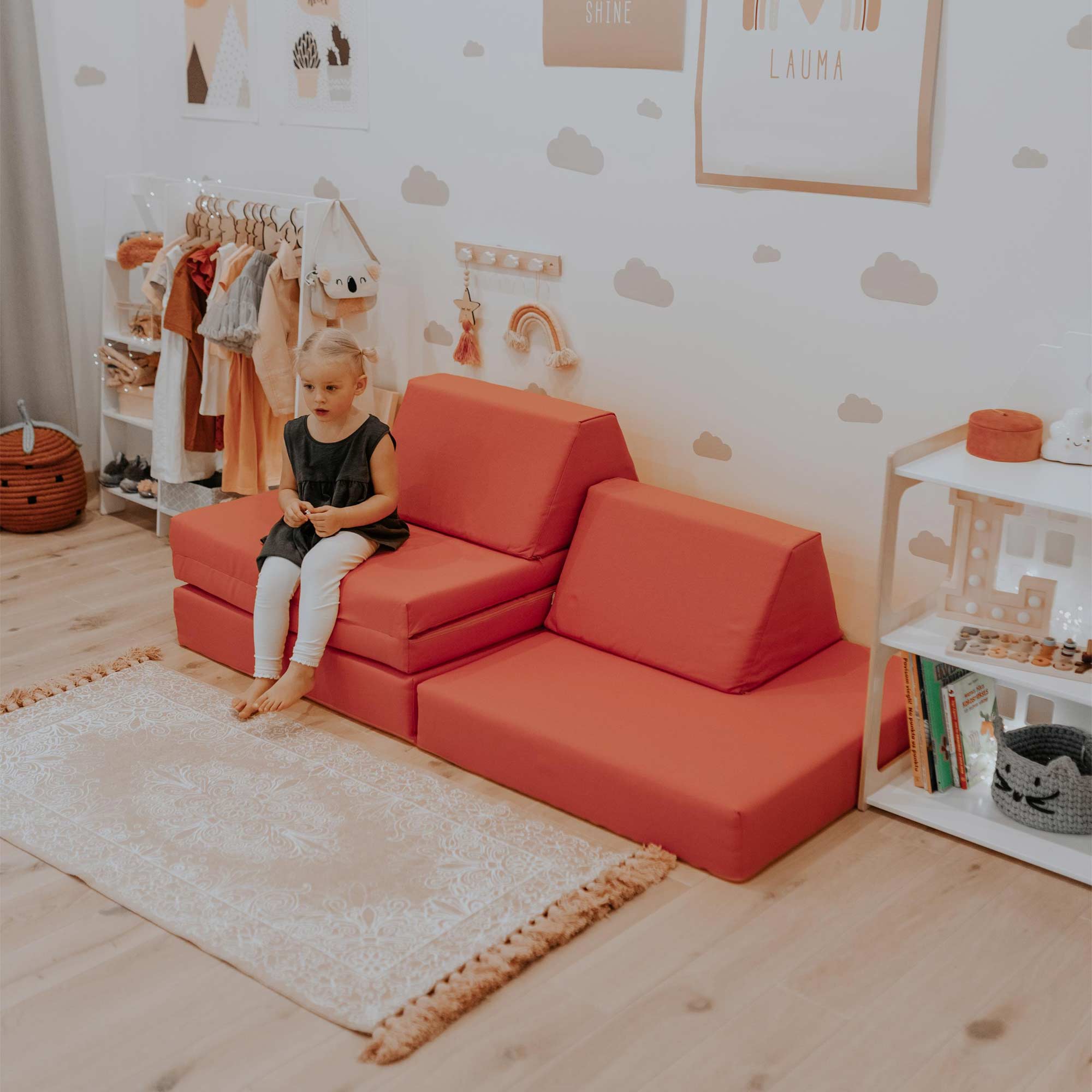 Toddler girl sitting on a coral Monboxy play sofa in her room
