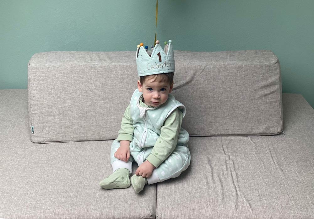 A baby boy in a blue crown, sitting on his grey Monboxy play sofa set