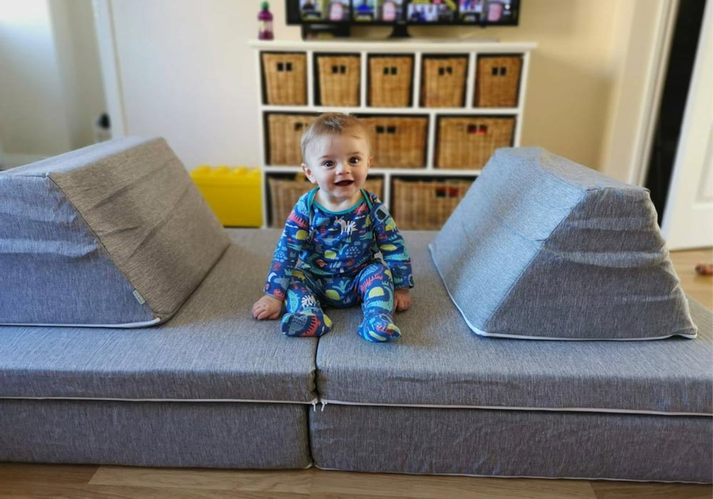 A baby sitting on a grey Monboxy play couch