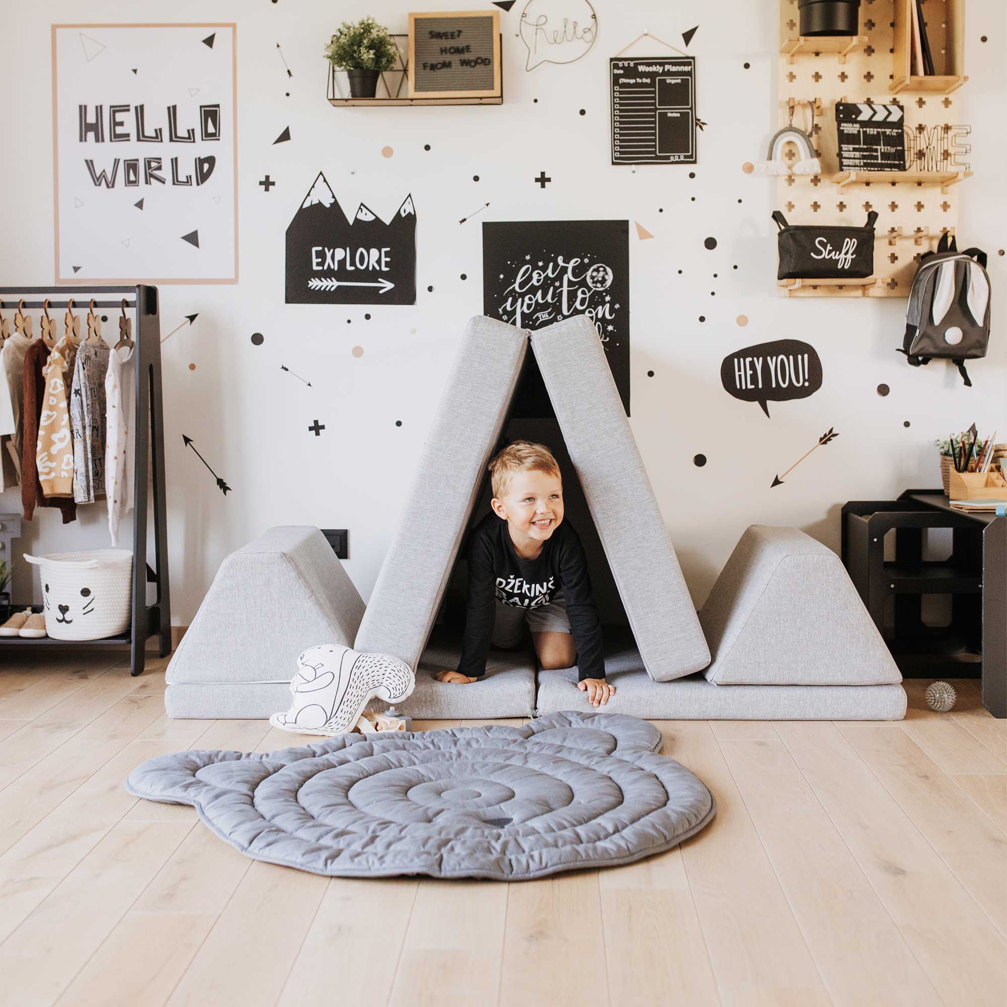 A happy boy inside his grey Montessori toy e.g. Monboxy play couch for kid put as a wigwam