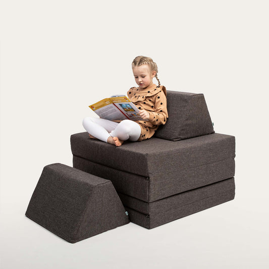 A girl reading a book while sitting on a brown play couch set