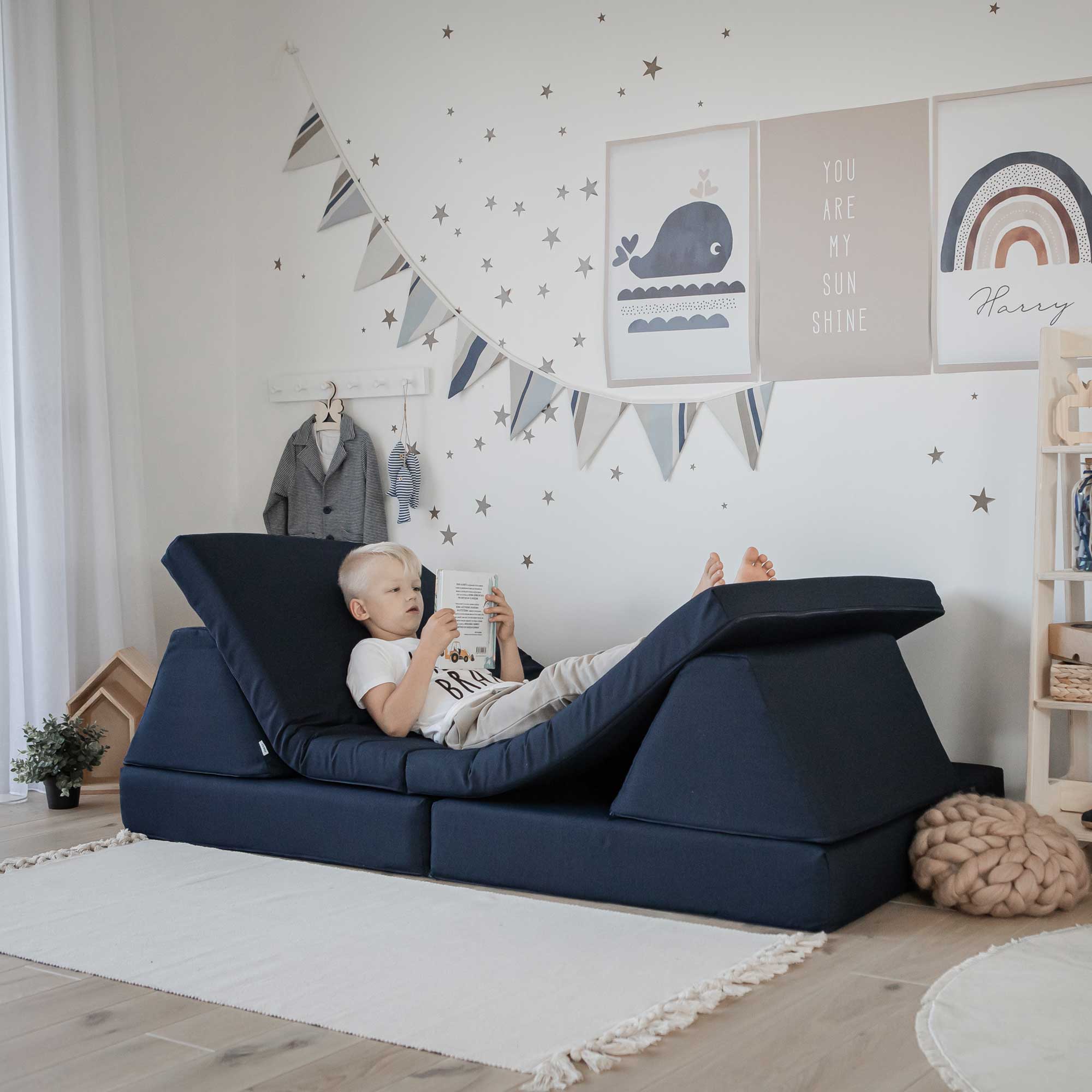 A boy laying down on his navy blue Monboxy play couch set and reading