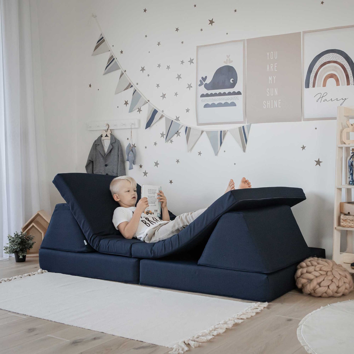 A boy relaxing and reading a book on his navy blue Monboxy play couch