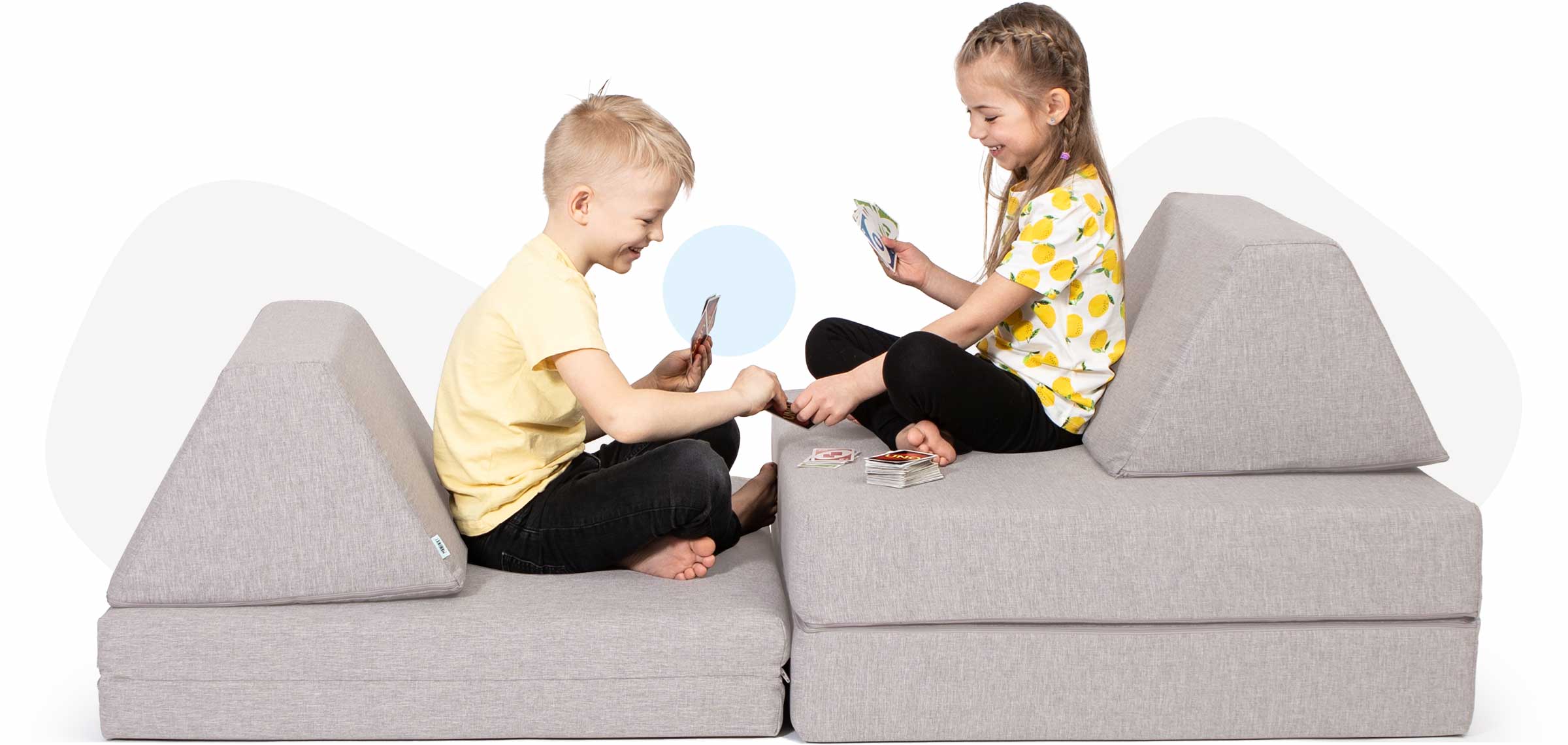 Kids sitting and playing cards on a beige Monboxy soft play sofa