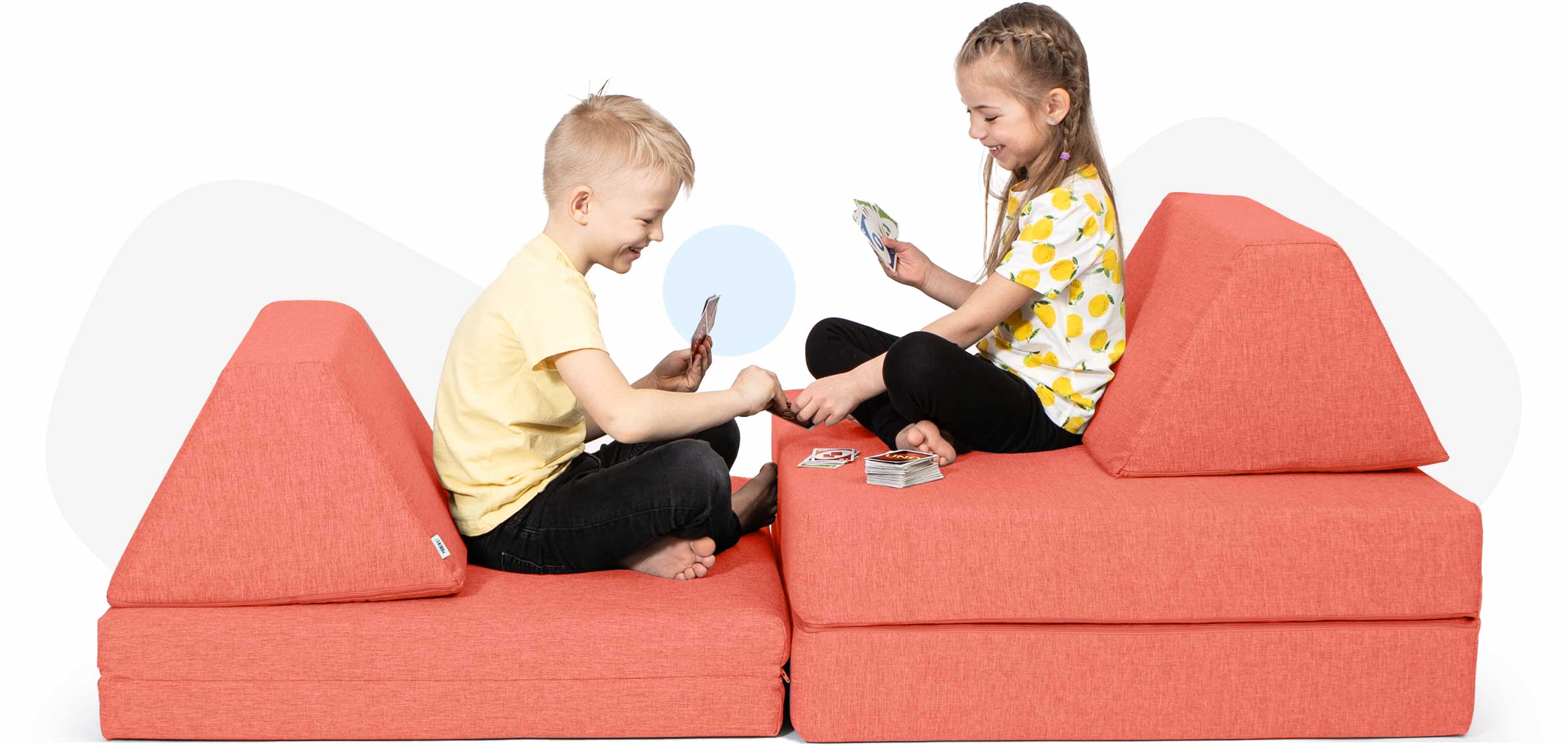Kids sitting and playing cards on a coral Monboxy sofa