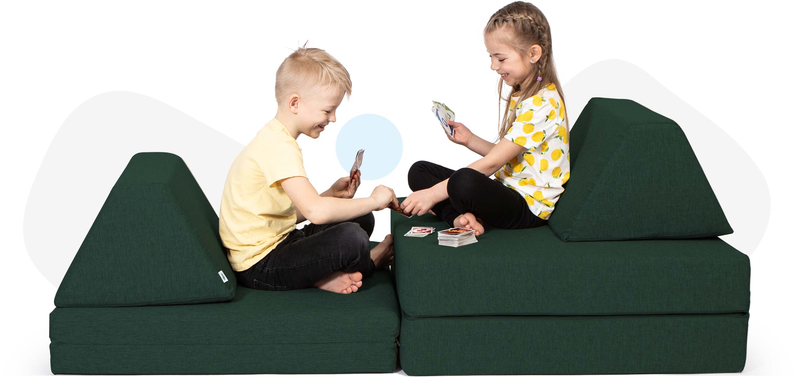Kids sitting and playing cards on a deep green Monboxy sofa