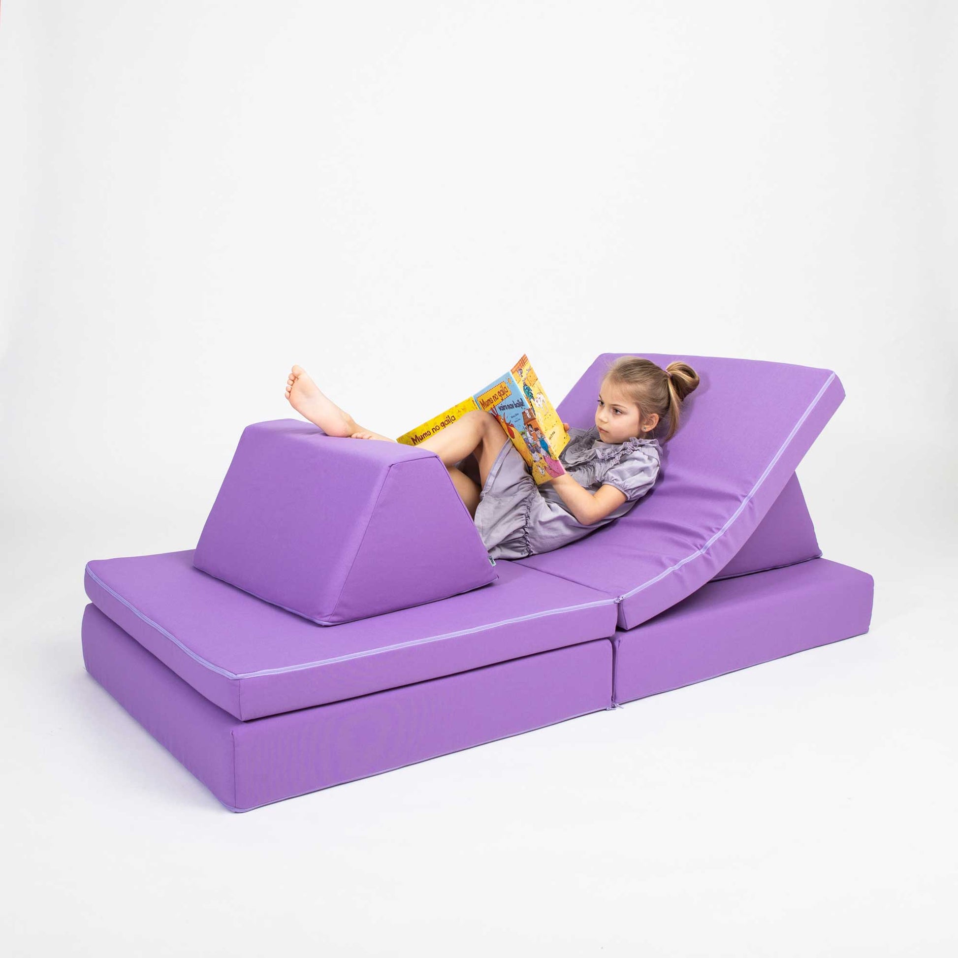 A girl laying down and reading on a purple Monboxy foam couch blocks set