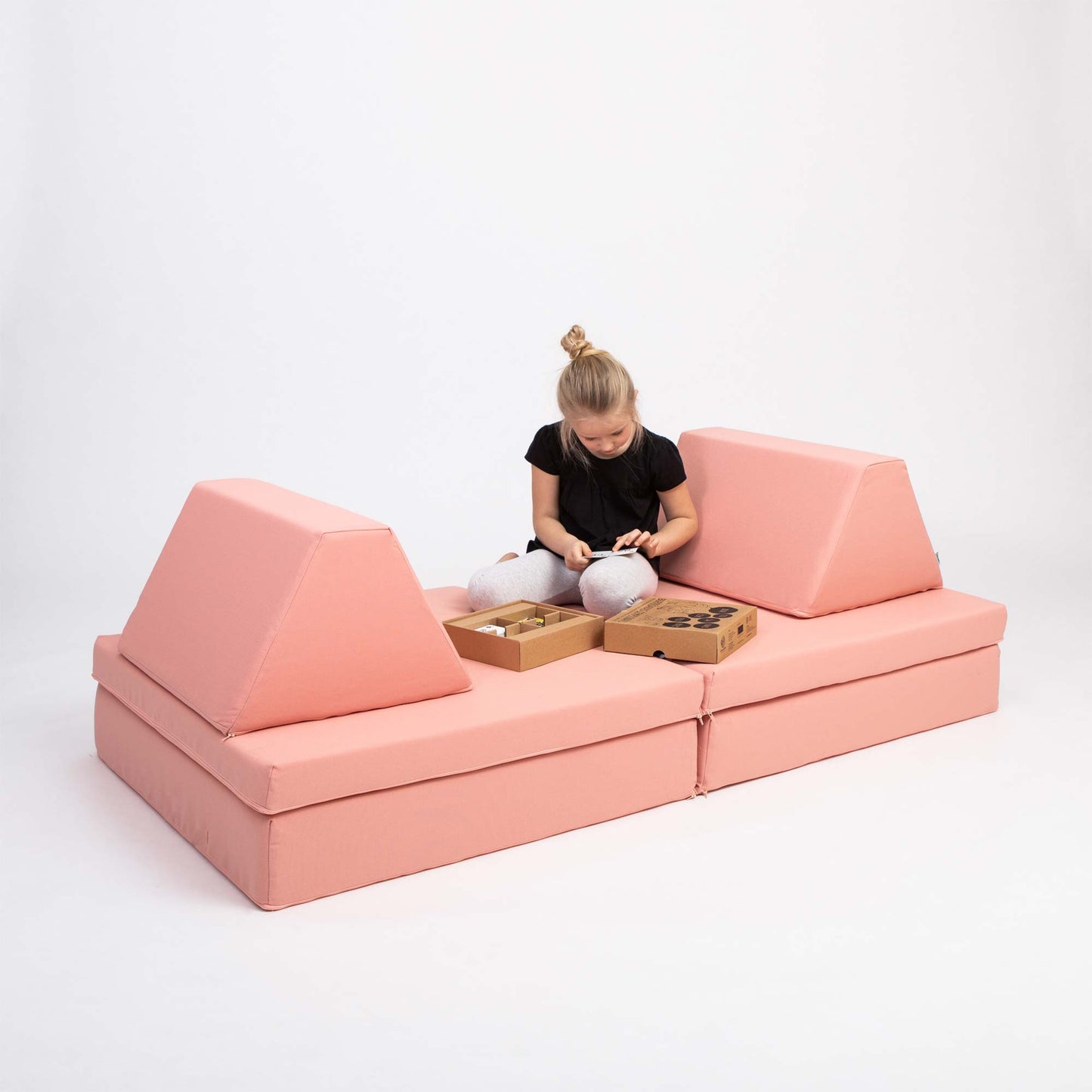 A girl playing with toys while sitting on her salmon pink Monboxy sofa