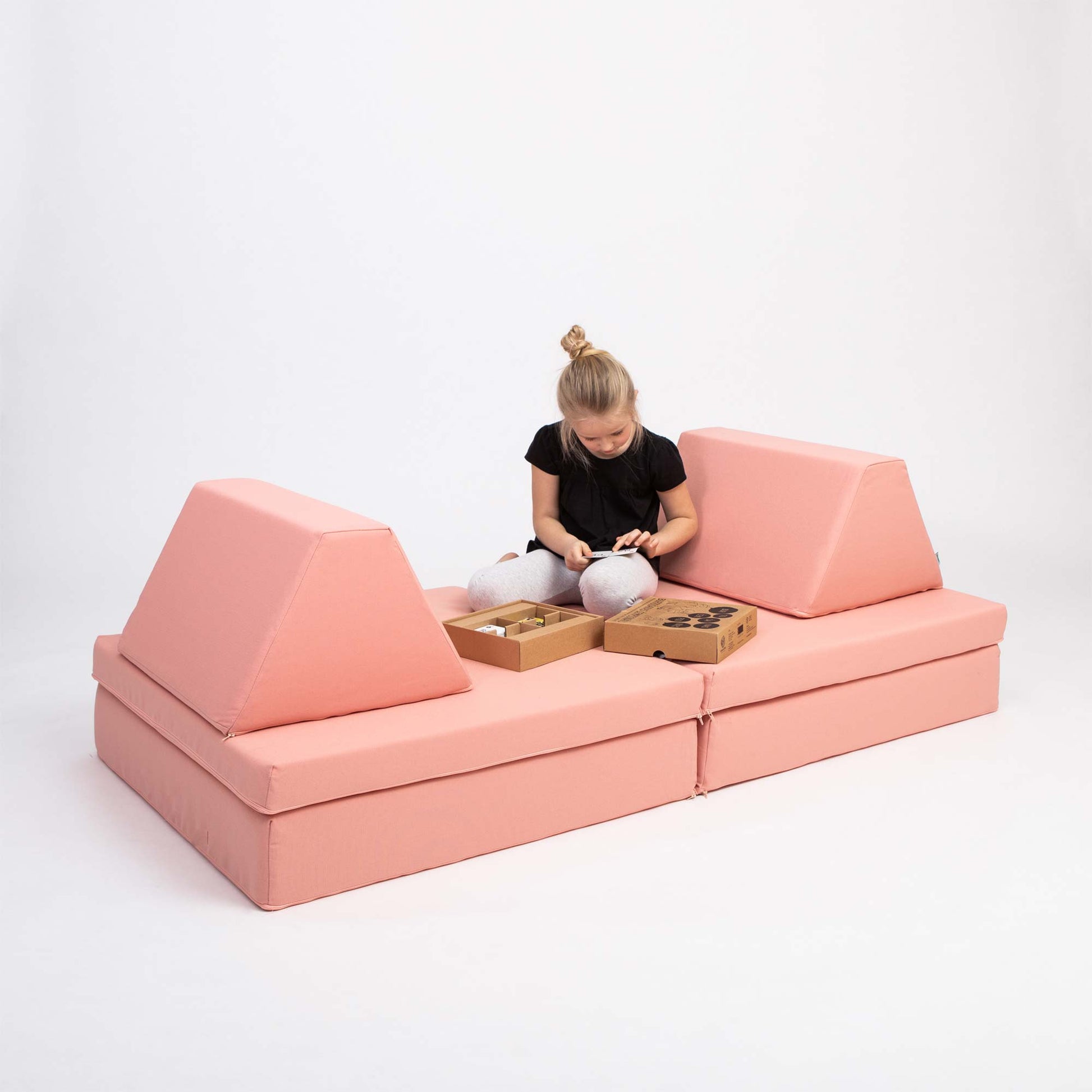 A girl playing with toys while sitting on her salmon pink Monboxy foam playset